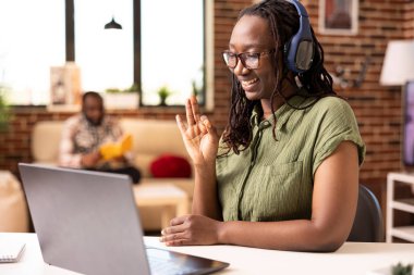 Smiling female entrepreneur giving approval gesture on selected items during virtual meeting with vendors. African american businesswoman with headphones, happily showing okay hand sign on video call.