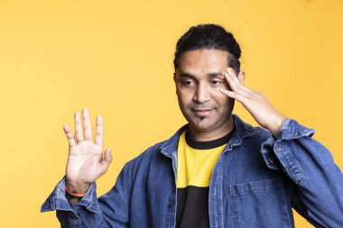 Dost canlısı bir adamın portresi. Arka planda ellerini sallıyor. Stüdyoda mutlu ve sakin görünüyor. Renkli giyinmiş, sırıtan ve rahat hisseden kendine güvenen şık Hintli..