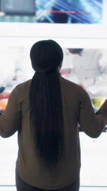 Vertical video User interacting with trending online videos feed on digital platforms. Woman looks at virtual video wall featuring global channels streaming dashboard with viral clips playlist, camera