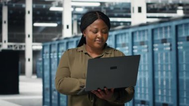 Programmer in data center using laptop to upgrade systems for increased stability. IT professional in server farm configuring infrastructure with notebook for optimum performance, camera B