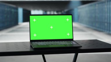 Green screen laptop in high tech data center facility with multiple rows of fully operational server racks. Mockup notebook used to oversee server hub built for digital storage systems