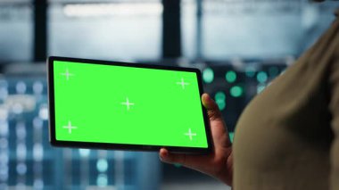 Close up of technician at work using green screen tablet in data center to check hardware for system stability. Employee using mockup device to oversee server farm and configure equipment, camera B