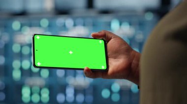 Server hub admin uses isolated screen smartphone to watch video tutorial on how to increase rigs workload capacity. Data center worker following guide on chroma key phone to improve speed, camera B