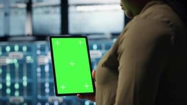 Admin with isolated screen tablet in data center implementing advanced power management solutions. Employee using chroma key device to oversee server hub, reducing energy consumption, camera B