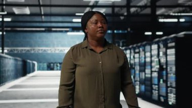 Software developer walking in data center, checking hardware for system stability. System administrator overseeing server farm room, monitoring infrastructure rigs, camera B