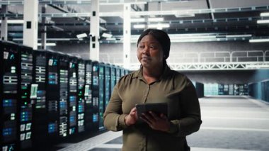 Veri merkezinde yürüyen yönetici, sistem istikrarı için yazılım güncellemelerini yönetmek için tablet kullanıyor. İdeal performans için altyapıyı ayarlayan sunucu çiftliği bilişim uzmanı, kamera A