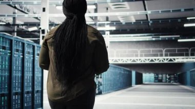 Woman walking through data center server rows, implementing advanced cooling and power management solutions. IT expert overseeing server farm, reducing energy consumption, camera A