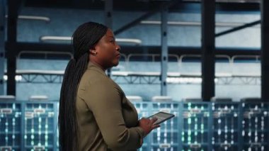 Smiling data center technician using tablet to manage software updates for system stability. Upbeat IT expert in server room configuring infrastructure with device for optimum performance, camera B