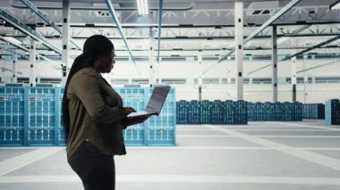 Dizüstü bilgisayarı olan teknisyen, veri merkezi sunucu sıralarını inceleyerek gelişmiş güç yönetimi çözümleri uyguluyor. İşçi sunucu merkezini denetlemek için dizüstü bilgisayar kullanıyor, enerji tüketimini azaltıyor, kamera A