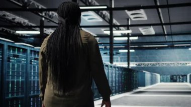 Data center system administrator oversees IT gear to maintain seamless operations. African american woman walks in server hub, doing network management for increased uptime, camera A