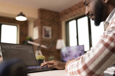 Focused software developer typing code on laptop during remote work session. IT freelancer working on app development and practicing software engineering data in home office environment.