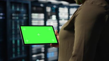 Data center programmer uses green screen tablet to develop disaster recovery plans, minimizing downtime. IT expert in server farm, enhancing data protection protocols using chroma key device, camera B
