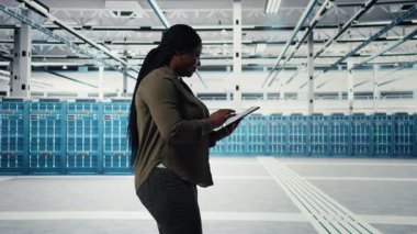 Developer in data center using tablet to upgrade systems for increase in clients workload capacity. IT expert in server farm configuring hardware, improving data processing speed, camera A