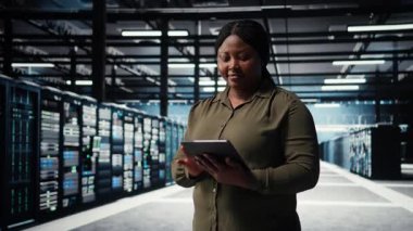 Programmer in data center using tablet to upgrade servers for increase in clients workload capacity. IT specialist in server farm configuring hardware rigs, improving data processing speed, camera A