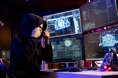 Hooded hacker in underground HQ doing ransomware attacks using AI to hold company systems hostage and demand money. Evil man using neural networks tech to hack enterprise networks, encrypting files