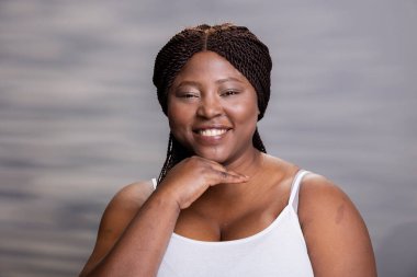 Afro-Amerikan portresi, doğal parlayan bir teni ve samimi bir gülümsemesi olan, kendine özgüveni ve kendine güveni vurgulamak için yeni ve pürüzsüz bir yüzle poz veren. Kendine güven.