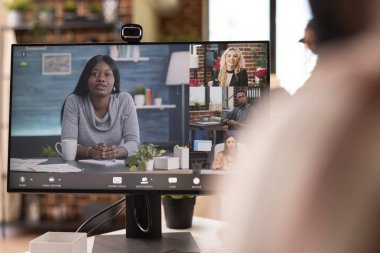 Remote financial advisor joins video call on desktop monitor, consulting with startup team from home. Professional seated at desk engages in virtual business discussion with multiple participants.