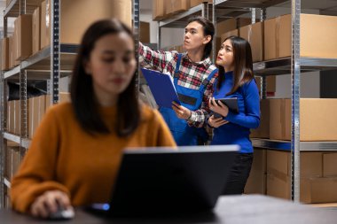 Asian workers team reviewing cargo inventory on shelving units at small warehouse, small scale local brand. Staff prepares taped boxes and manages delivery in a well organized shipping area.