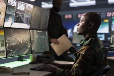 Terörle Mücadele Birimi ajanı kamuflaj üniforması giyip düşman konumunu tespit etmek için hedef alma teknolojisini kullanıyor. Savunma güvenlik uzmanı tehlikeli tehditleri takip etmek için uydu donanımı kullanıyor