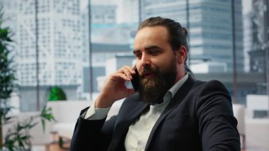 CEO multitasking and managing an important phone call with investors while he reviews financial reports on his laptop. Strategic decision making in corporate life at the workplace. Camera B.