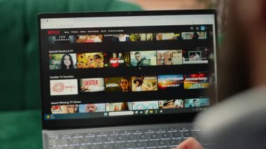 Bucharest, Romania - July 30th 2024 - Business CEO browsing Netflix streaming platform in his office, looking for a good movie or tv show to kill time at work. Successful entrepreneur. Camera B.