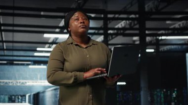 Supervisor in data center using laptop to coordinate deployment of new server architecture. Server farm IT specialist using notebook to do rollout of cybersecurity framework, protecting data, camera B