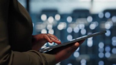 Data center programmer uses tablet to develop disaster recovery plans, minimizing downtime. IT professional walking in server farm, enhancing data protection protocols using device, camera B