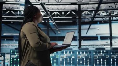 Admin in data center using app on laptop to ensure error free rigs networks for intense computational demands. IT expert uses notebook to monitor server hub gear components for failures, camera A