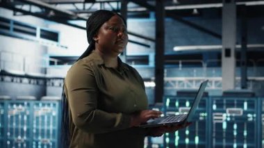 Admin in data center using app on laptop to ensure error free rigs networks for intense computational demands. IT expert uses notebook to monitor server hub gear components for failures, camera B