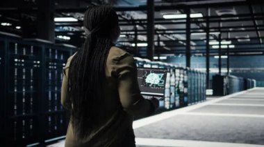 Veri merkezi mühendisi, işlem verimliliğini optimize etmek için dizüstü bilgisayarda derin öğrenme kullanıyor. Uzman donanım hızlandırıcı karmaşık yapay zeka hesaplamalarıyla sunucu odasında çalışan bilişim uzmanı, kamera A