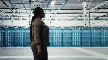 Veri merkezi yönetimi siber tehditlere ve savunmasızlıklara karşı güvenlik denetimleri yapıyor. Sunucu odasında yürüyen kadın, endüstri standartlarına uymayı garanti ediyor, kamera A