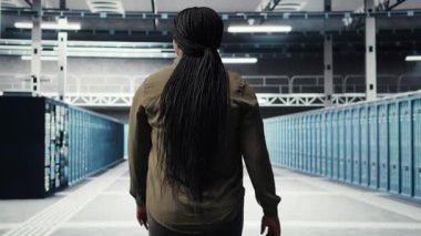 Veri merkezi sunucu sıralarında yürüyen bir kadın, sistem dengesi için ekipmanları kontrol ediyor. Bilgi İşlem Uzmanı sunucu çiftliği denetleme, altyapı ana bilgisayarlarını izleme, kamera A