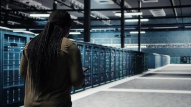High tech data center technician uses tablet to develop disaster recovery plans, minimizing downtime. IT employee walking in server room, enhancing data protection protocols using device, camera A