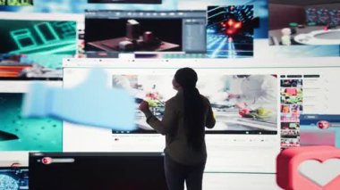 Kullanıcı dijital platformlardan beslenen trend çevrimiçi videolarla etkileşime geçiyor. Kadın, küresel kanalların viral klipler çalma listesi ve kamera A ile gösterge panelini gösteren sanal video duvarına bakıyor.