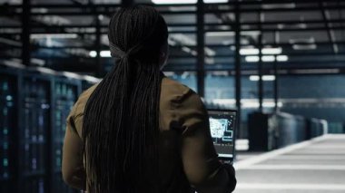 Veri merkezi mühendisi, işlem verimliliğini optimize etmek için dizüstü bilgisayarda derin öğrenme kullanıyor. Uzman donanım hızlandırıcı karmaşık yapay zeka hesaplamalarıyla sunucu odasında çalışan bilişim uzmanı, kamera B