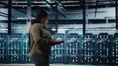 Software developer in data center using laptop to coordinate deployment of new server architecture. Server hub IT professional using notebook to do rollout of cybersecurity framework, camera A