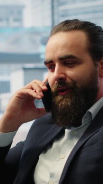 Vertical Video CEO multitasking and managing an important phone call with investors while he reviews financial reports on his laptop. Strategic decision making in corporate life at the workplace