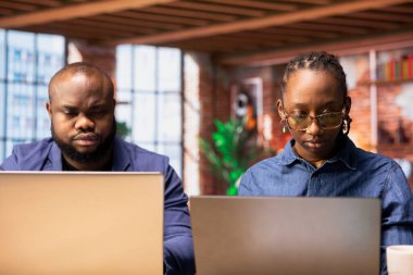 Black people both working from home at their designated office, using online digital tools on computers for tasks management. Completing operations efficiently from their comfortable house.