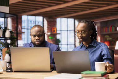 Afrika kökenli Amerikalı erkek ve kadın, işverenleri için önemli bir projeyi bitirmek için dizüstü bilgisayarları üzerinde birlikte çalışıyorlar. ortaklar ve istemcilerle ağ kurma.