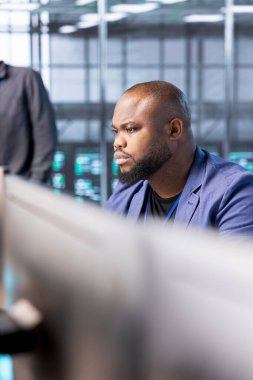 Veri merkezindeki Afrikalı Amerikalı mühendis yüksek işlemci kullanımı nedeniyle PC kullanarak sunucu performans sorunlarını kontrol ediyor. Sunucu çiftliğindeki adam yetersiz hafıza hatalarını düzelterek donanımı yavaşlatıyor