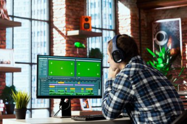 Remotely working videographer at home doing video montage using specialized software applications on green screen PC. Video editor using editing tools on mockup computer to cut movie project footage