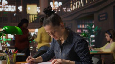 Kütüphaneci, akademik başarısı olan öğrencilere yardım etmek ve kütüphanede özel derslere hazırlanmak için öğrenim materyalleri notlarını tamamlıyor. Okur yazarlığı ve eğitimi destekleyen pedagoji uzmanı. Kamera A.