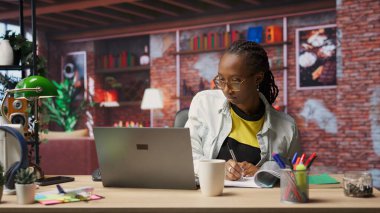 Merkez ofisteki muhasebeci dizüstü bilgisayardaki mali raporları inceliyor ve bilgi yazıyor. Dairede telgraf işçisi, defter üzerindeki belgeleri okuyor ve kağıda kalemle notlar alıyor, B kamerası.