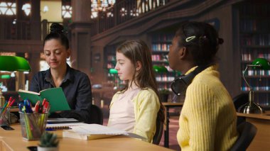 İlkokul öğrencileri, okul kütüphanesindeki çeşitli öğrenim ortamlarında ev ödevleri üzerinde çalışan bir öğretmenden destek alıyorlar. Profesör dersten önce öğrencilerine rehberlik ediyor. Kamera A.