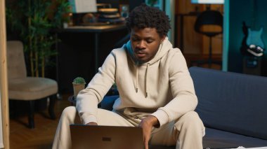 Evde bir iş projesi için çevrimiçi araştırma yapan odaklanmış bir adam, kahve masasında dizüstü bilgisayarıyla oturuyor ve internette makaleler okuyor. Web sayfalarında sörf yapan ve veri toplayan kişi. Kamera A.