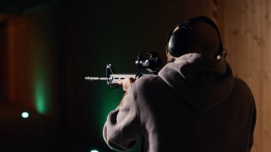 Atış poligonu müşterisi yarı otomatik silahla hedefleri vuruyor, eğleniyor. Kapalı alanda ateş eden bir adam boğa güreşçilerine tüfekle ateş ediyor, koruma ekipmanları takıyor, kamera B