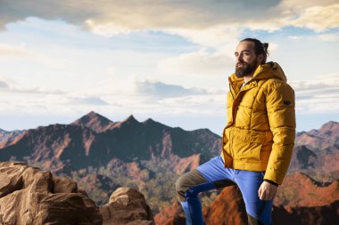 Kararlı gezgin, panoramik manzaranın macera ve kişisel gelişimi temsil ettiği bir dağ zirvesinin yalnızlığının tadını çıkarıyor. Açık hava teçhizatıyla yürüyüşçü rüzgarlı dağın tepesinde üşüyor..