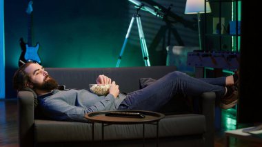 Neşeli ev sahibi kanepeye uzanıyor, TV 'de film izliyor, komik sahnelerle eğleniyor. Ev sinemasında eğlenen, iyi filmler izleyen, patlamış mısır yiyen, kamera A 'da mutlu bir adam.