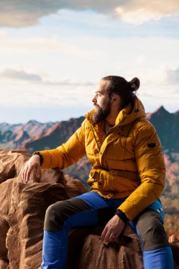 Kararlı dağcı dağların manzarasına hayran olmak için duraklıyor ve engin bir gökyüzü nefes kesici bir zemin oluşturuyor. Erkek yürüyüşçü doğa keşfi ve macerası için yürüyüş yapıyor..
