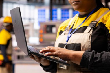 Closeup of technician ensuring smooth operation of automated production line, using software on laptop. African american industrial specialist optimizes manufacturing processes in smart factory.